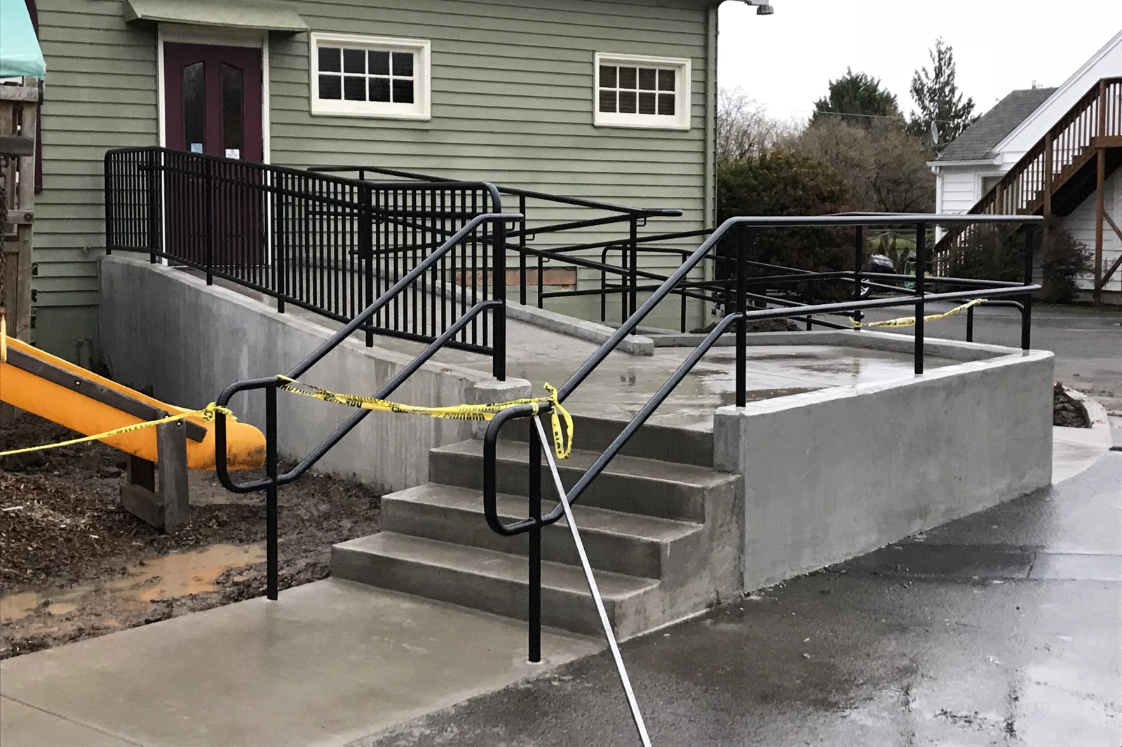 A custom-fabricated black steel ADA-compliant commercial railing system featuring continuous handrails and picket guardrails, providing safe, accessible entry for a concrete ramp and staircase.