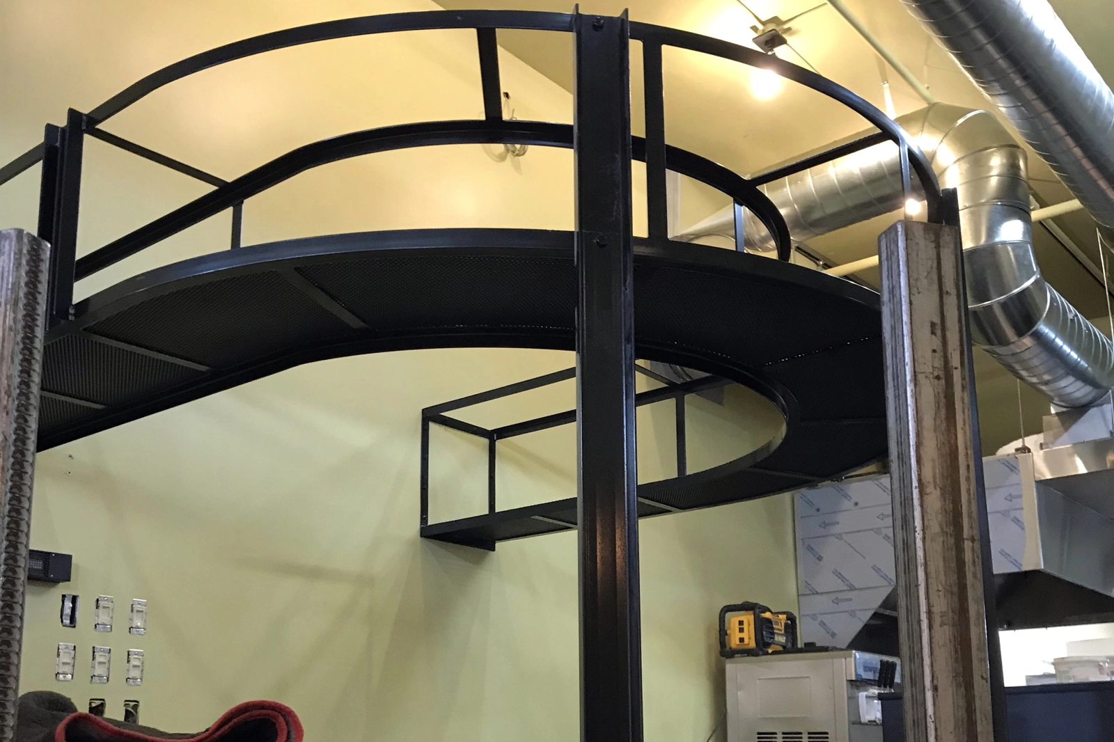 A custom-fabricated black steel mezzanine platform with safety guardrails, installed in an industrial-style interior with exposed ductwork. | Chip and Dale's Iron Works
