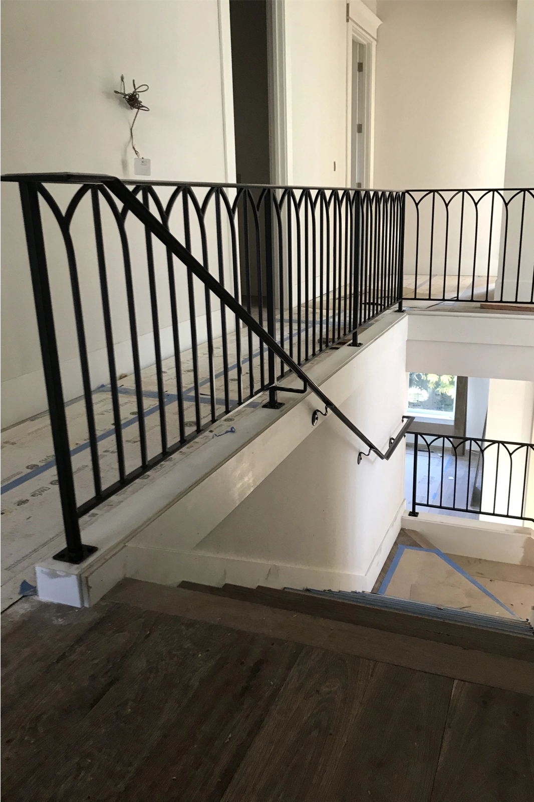 Black wrought iron stair railing with a unique gothic-inspired arched picket design, installed on a residential staircase and mezzanine.