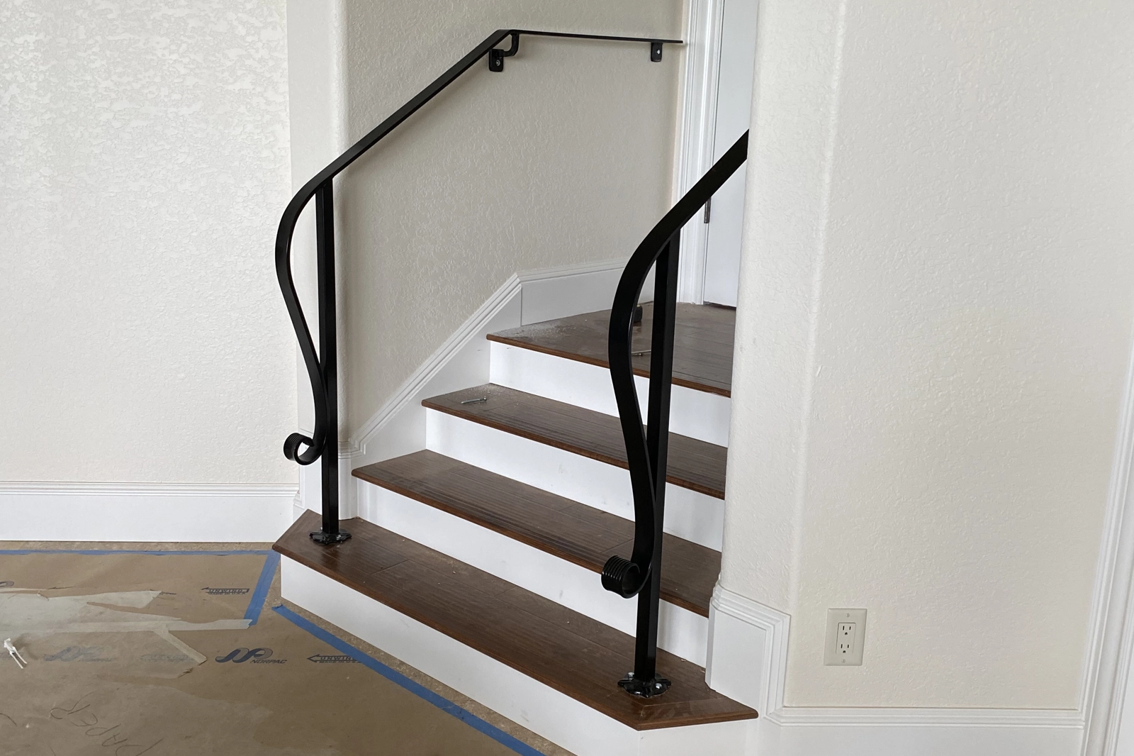 A custom-handcrafted residential interior stair railing featuring black wrought iron with elegant hand-forged S-curve posts and decorative scrollwork finials.