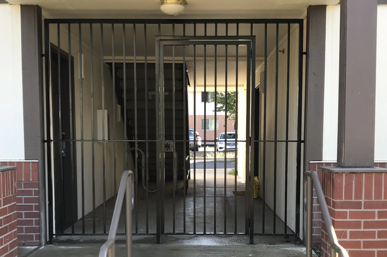 A custom-fabricated black steel security gate with a central pedestrian door and vertical pickets, installed in a commercial apartment building breezeway.