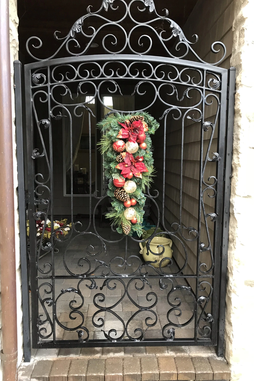 A custom-fabricated black wrought iron gate with intricate scrollwork and a decorative arch, adorned with a festive red and green Christmas swag wreath.