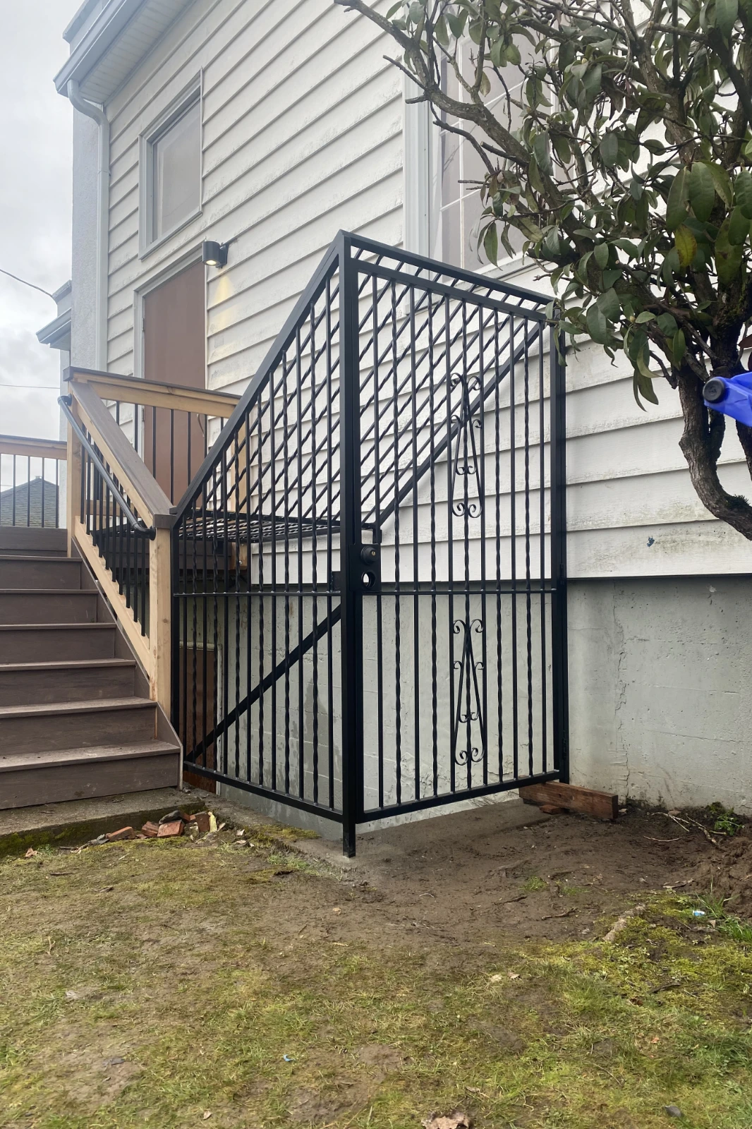 A custom-fabricated black wrought iron security enclosure with a tall pedestrian gate and twisted metal pickets, surrounding an exterior basement stairwell on a residential home.