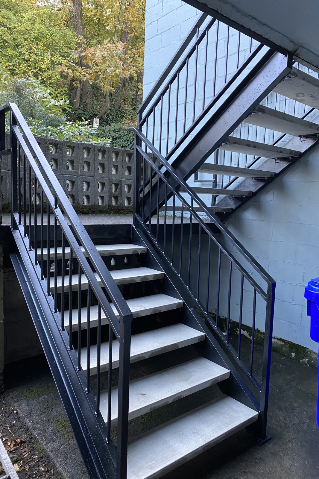 A custom-fabricated black steel staircase, featuring light gray concrete treads and a matching modern metal picket railing system.